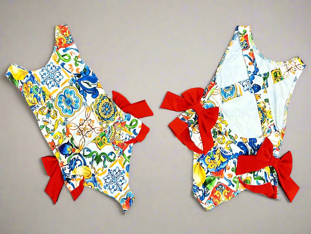 Baby and toddler girl’s colourful one-piece swimsuit with red side bows, perfect for summer holidays, beachwear, and poolside fun